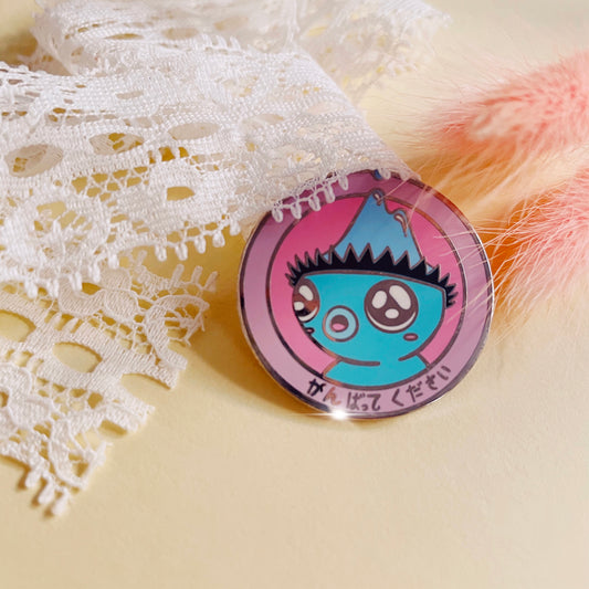 dazed kappa pin in front of white lace and pink foxtail plants. pin features a confused looking turquoise kappa (japanese water spirit) inside two pink circles. hiragana on the border reads ‘try hard please’.